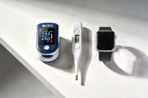 家用健康监测设备：便携式血氧仪、电子体温计和心率手环陈列在简约桌面上