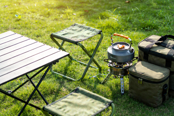 轻便型户外露营装备：折叠桌椅、便携炊具和收纳包整齐摆放于草地上